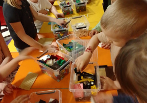 Motylki zgromadzone wokół stołu budują z klocków Lego. Na stole pojemniki z klockami Lego.