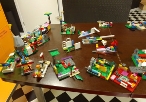 Na dużym stole prezentują się budowle z klocków Lego wykonane przez dzieci.