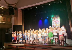 Na scenie stoją wszystkie dzieci, które zostały nagrodzone w konkursie wokalnym i śpiewają piosenkę "Niedorosłe piosenki".