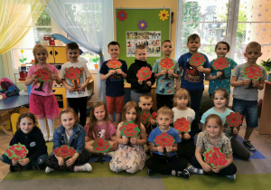 Dzieci z grupy "Słoneczek" stoją na tle tablicy i trzymają w rękach laurki w kształcie drzewek.