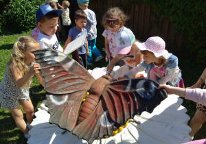 Dzieci oglądają rzeźbę motyla - Rusałki Pawika usytuowaną na białej stokrotce.