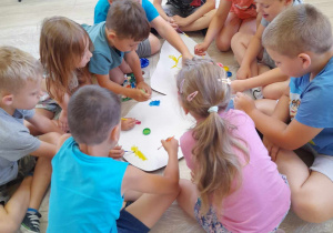 Dzieci z grupy "Słoneczka" siedzą na podłodze i ozdabiają farbami skrzydło motyla z kartonu.