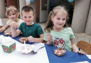 Oliwia, Krzysio i Ala K. z uśmiechami na twarzy zjadają pyszny lodowy deser.