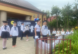 "Słoneczka" ustawione na tarasie przedszkolnym śpiewają piosenkę "Hej przedszkole".