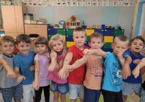 Dzieci z grupy "Słoneczek" stoją w rzędzie z wyciągniętymi rączkami. Przedszkolaki pokazują stempelki jakie otrzymały za udział w zajęciach.