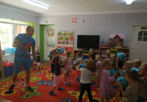 Dzieci wraz z instruktorem maszerują po sali trzymając piłki.