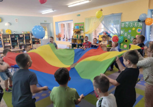 Dzieci trzymają chustę animacyjną, na której podrzucają balony.