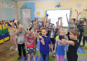 Przedszkolaki stoją na dywanie. W dłoniach trzymają kolorowe papierowe kropki.