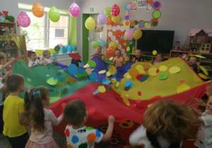 Dzieci podczas zabawy z chustą, na której znajdują się kolorowe kropki.