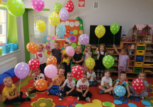 Zdjęcie grupowe z kolorowymi balonami w kropki na tle dekoracji.