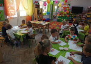 Dzieci przy stoliku wykonują pracę plastyczną - stemplują paluszkami kolorowe kropki.