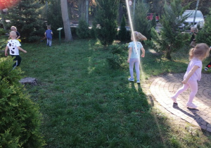 Dzieci swobodnie biegają w ogrodzie przedszkolnym i szukają kolorowych kropek.