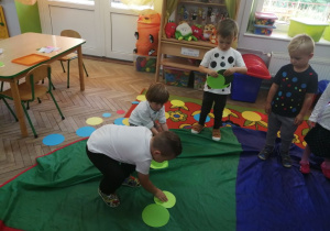 Grupka dzieci stoi na chuście animacyjnej i kładzie na niej zielone kropeczki.