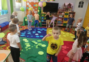 Dzieci ustawione w kole stoją przed chustą animacyjną, na której leżą kolorowe kropeczki.