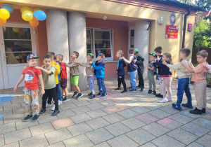 Dzieci z grupy IV stoją ustawione "w pociąg" na tarasie przedszkolnym tańcząc do piosenki "Jedzie pociąg z daleka".