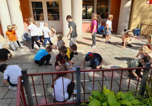 Dzieci rysują kredą na tarasie przedszkolnym.