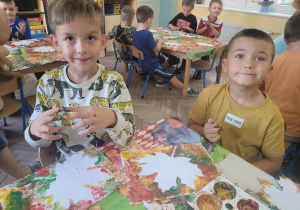 Julek i Gabryś siedząc przy stoliku tworzą jesienną pracę plastyczną z wykorzystaniem farb.
