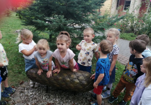 Grupka dzieci stoi przy rzeźbie szyszki.