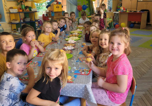 Dzieci siedzą przy stole nakrytym słodkimi pysznościami.