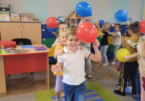 Dzieci ustawione w pociąg tańczą z kolorowymi balonami w dłoniach.