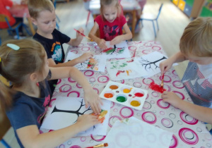 Grupa dzieci ozdabia kolorową farbą sylwety drzew z wykorzystaniem folii bąbelkowej.