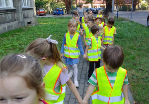 Grupa "Biedronek" w odblaskowych kamizelkach rusza spod przedszkola na skrzyżowanie.