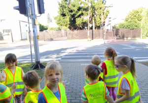 Dzieci przygotowują się do przejścia na drugą stronę ulicy i czekają na zmianę światła na zielone.