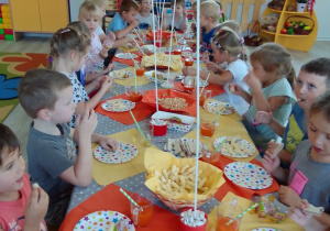 Biedronki siedzą przy długim stole, na którym są: kolorowe serwetki, talerzyki, balony na patyczkach i słodycze