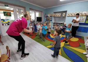 Maluszki na dywanie z panią Grażyną starają się naśladować ruchy, które pokazuje pani instruktor.