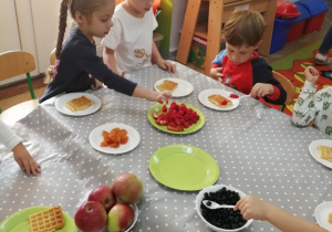 Amanda, Fabian i Staś przy stoliku nakładają na gofry owoce.