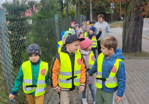 Dzieci z grupy Słoneczek ubrane w kamizelki odblaskowe idą na pobliski przystanek autobusowy