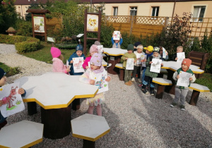 Zdjęcie grupowe dzieci z pracami plastycznymi przy stolikach w kształcie plastra miodu .