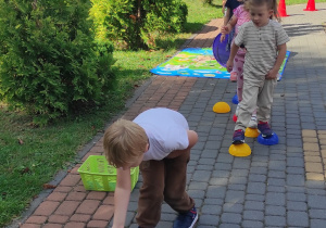 Adaś wrzuca woreczek do obręczy, wojtek przechodzi po krążkach, reszta dzieci porusza się za nimi