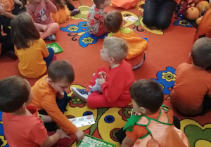 Dzieci siedzą na dywanie w małych grupkach podczas zabawy w bingo.