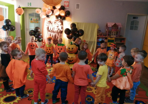 Dzieci ustawione w kole podczas zabawy integracyjnej "Kręci się dynia". W tle dekoracja z okazji Dnia dyni.
