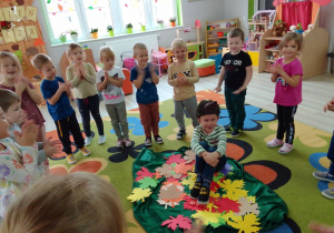 Biedronki podczas zabawy kołowej w „Jeżyka”, w środku koła na kolorowych liściach z maską jeża siedzi Antek.