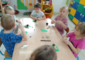 Dzieci przy stolikach konstruują z gliny i szyszek jeża.