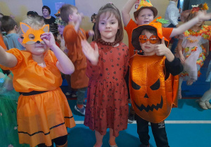 Przedszkolaki w jesiennych strojach radośnie tańczą obok siebie przy muzyce.