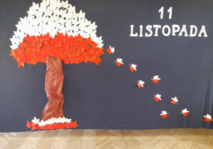 Dekoracja z okazji Narodowego Święta Niepodległości. Na granatowym tle przypięte jest drzewo z biało-czerwoną koroną i spadające oraz napis 11 Listopada.