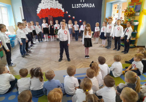 Dzieci stoją w galowych strojach w półkolu, a na środku sceny stoi Franek z Zosią. Przedszkolaki śpiewają piosenkę "Nasza Polska".