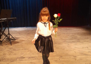 Zosia kłania się na scenie po występie. Dziewczynka trzyma dwie róże - białą i czerwoną.