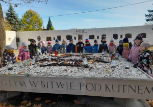 Dzieci stoją wokół płyty upamiętniającej Żołnierzy Poległych w bitwie pod Kutnem. W tle "Mur pamięci" z tablicami pamiątkowymi.
