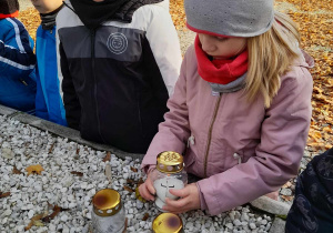 Lena kładzie znicz na płycie upamiętniającej Żołnierzy Poległych w bitwie pod Kutnem. Obok stoi Franek i Tymon.