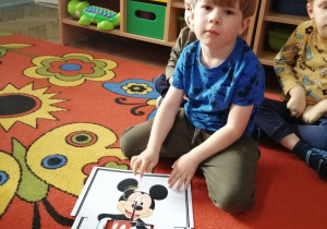 Staś siedzi na dywanie, a przed nimi leży ułożony z części obrazek z Myszką Mickey.