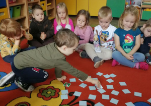 Dzieci siedzą na dywanie przed nimi rozłożone memory, Bartek wybiera obrazki.