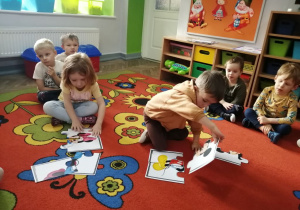 Emma i Mikołaj na dywanie układają puzzle z Myszką Mickey.