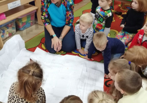 Dzieci na dywanie wspólnie z Panią oglądają rozłożony wykrój bluzki.