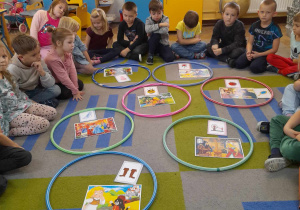 Dzieci siedzą na dywanie, a na środku leżą w obręczach obrazki z bajek oraz dopasowanych do nich rekwizytów. "Słoneczka" prezentują wykonane przez siebie zadanie.