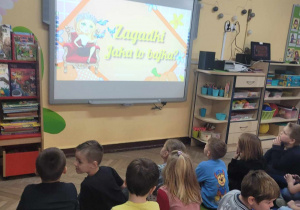 Dzieci z grupy "Słoneczek" rozwiązują bajkowe zagadki na tablicy multimedialnej.