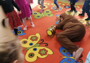 Dzieci idą w kole trzymając się za ręce, podczas zabawy „Stary niedźwiedź mocno śpi”, a na środku koła leży nauczyciel w stroju misia.